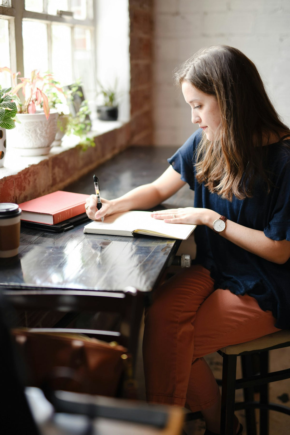 Woman sitting by a bright window writing her goals in a notebook