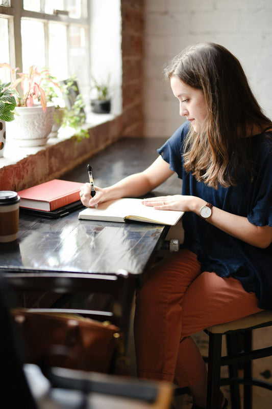 Woman sitting by a bright window writing her goals in a notebook