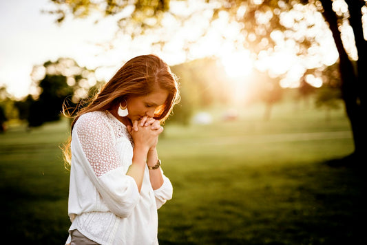 Woman praying peacefully beside a tree in soft natural light