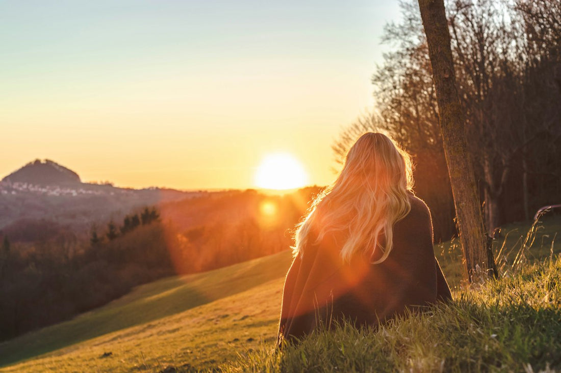 Woman sitting on green grass looking toward the warm sun